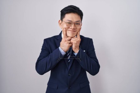 Téléchargez les photos : Jeune homme asiatique portant costume d'affaires et cravate souriant avec la bouche ouverte, les doigts pointant et forçant sourire joyeux - en image libre de droit