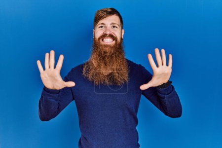 Photo for Redhead man with long beard wearing casual blue sweater over blue background showing and pointing up with fingers number ten while smiling confident and happy. - Royalty Free Image