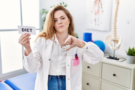 Photo for Young caucasian woman working at rehabilitation clinic holding diet banner with angry face, negative sign showing dislike with thumbs down, rejection concept - Royalty Free Image