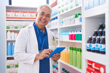 Téléchargez les photos : Homme moyen aux cheveux gris pharmacien utilisant un pavé tactile travaillant à la pharmacie - en image libre de droit