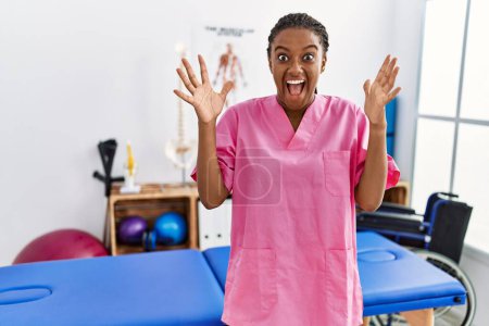Photo for Young african american woman working at pain recovery clinic celebrating crazy and amazed for success with arms raised and open eyes screaming excited. winner concept - Royalty Free Image