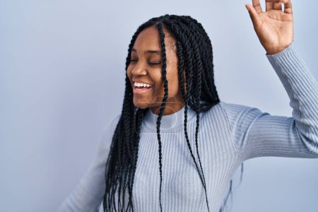 Foto de Mujer afroamericana de pie sobre fondo azul bailando feliz y alegre, sonriente moviéndose casual y confiado escuchando música - Imagen libre de derechos