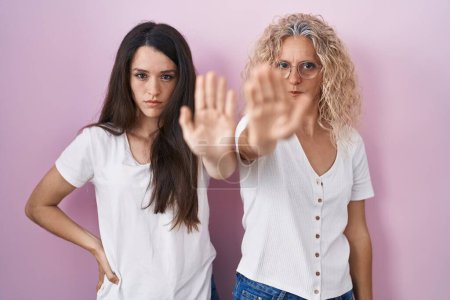 Photo for Mother and daughter standing together over pink background doing stop sing with palm of the hand. warning expression with negative and serious gesture on the face. - Royalty Free Image