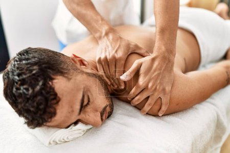 Photo for Two hispanic men physiotherapist and patient having rehab session massaging back at beauty center - Royalty Free Image