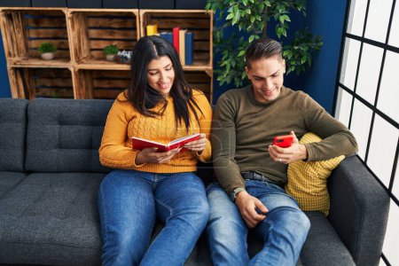 Foto de Hombre y mujer pareja usando teléfono inteligente y libro de lectura en casa - Imagen libre de derechos