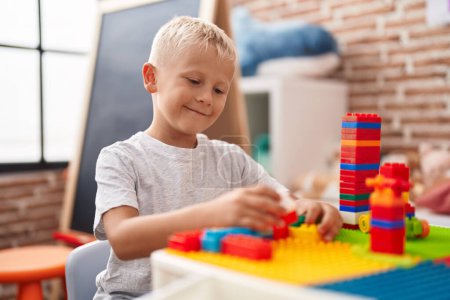 Photo for Adorable toddler playing with construction blocks sitting on table at classroom - Royalty Free Image
