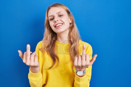 Foto de Young caucasian woman standing over blue background showing middle finger doing fuck you bad expression, provocation and rude attitude. screaming excited - Imagen libre de derechos