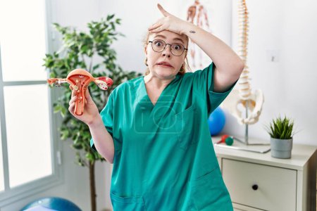 Photo for Young redhead doctor woman holding anatomical model of female genital organ stressed and frustrated with hand on head, surprised and angry face - Royalty Free Image