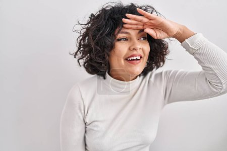 Photo for Hispanic woman with curly hair standing over isolated background very happy and smiling looking far away with hand over head. searching concept. - Royalty Free Image
