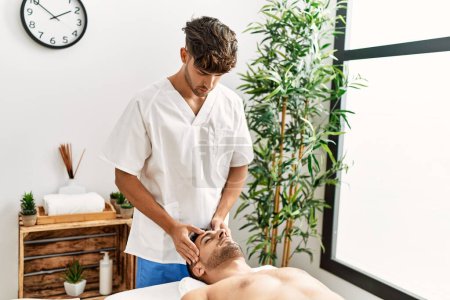 Téléchargez les photos : Deux hommes hispaniques thérapeute et patient ayant massage facial au centre de beauté - en image libre de droit