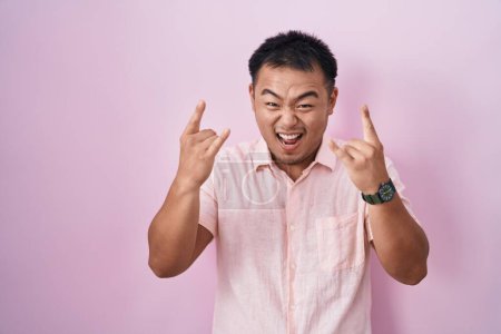Photo for Chinese young man standing over pink background shouting with crazy expression doing rock symbol with hands up. music star. heavy music concept. - Royalty Free Image