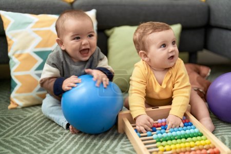 Photo for Two toddlers playing with balls and abacus sitting on floor at home - Royalty Free Image