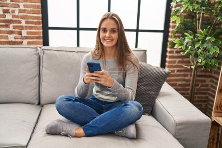 Photo for Young blonde woman smiling confident using smartphone at home - Royalty Free Image
