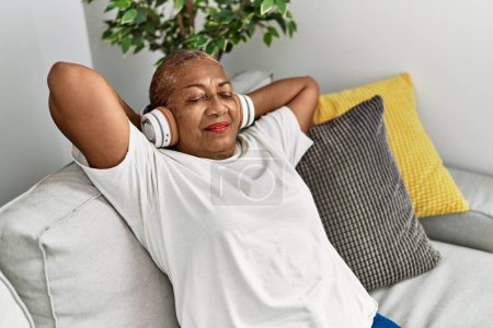 Foto de Mujer afroamericana mayor sonriendo confiada escuchando música en casa - Imagen libre de derechos