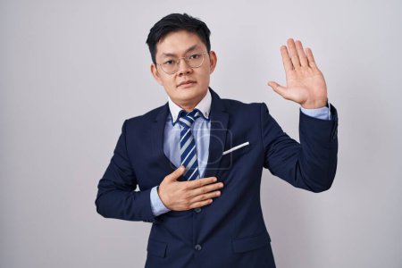 Photo for Young asian man wearing business suit and tie swearing with hand on chest and open palm, making a loyalty promise oath - Royalty Free Image