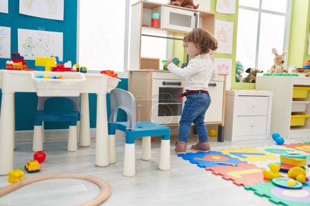 Foto de Adorable chica hispana jugando con la cocina de juego de pie en el jardín de infantes - Imagen libre de derechos