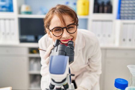 Téléchargez les photos : Jeune femme caucasienne portant l'uniforme de scientifique utilisant le microscope au laboratoire - en image libre de droit