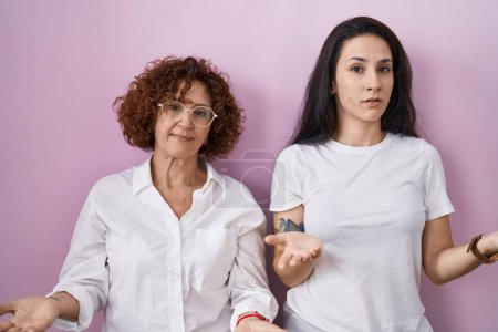 Téléchargez les photos : Hispanic mother and daughter wearing casual white t shirt over pink background clueless and confused with open arms, no idea concept. - en image libre de droit