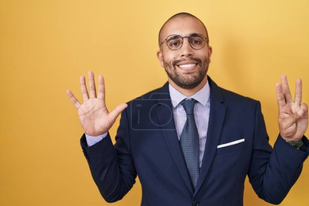 Foto de Hispanic man with beard wearing suit and tie showing and pointing up with fingers number eight while smiling confident and happy. - Imagen libre de derechos