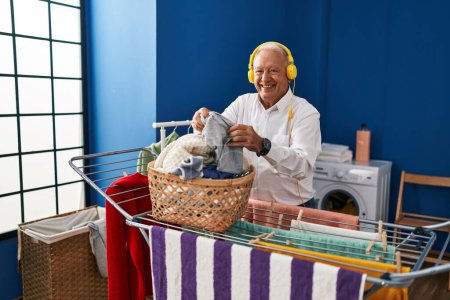 Foto de Senior man listening to music hanging clothes on clothesline at laundry room - Imagen libre de derechos