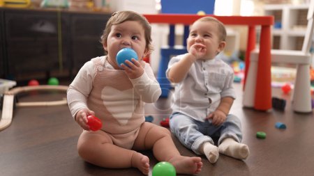 Foto de Dos niños pequeños chupando bolas sentados en el suelo en el jardín de infantes - Imagen libre de derechos