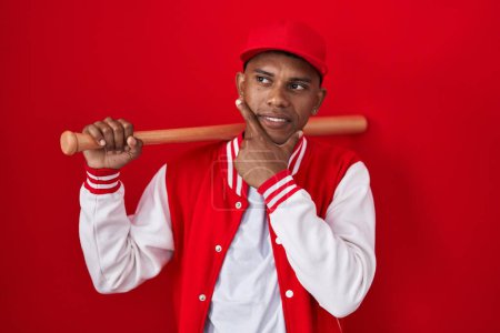 Photo for Young hispanic man playing baseball holding bat thinking worried about a question, concerned and nervous with hand on chin - Royalty Free Image