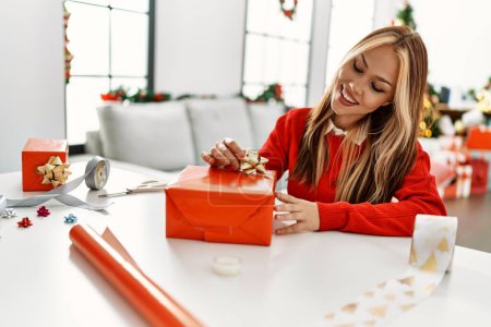 Téléchargez les photos : Jeune femme caucasienne préparant cadeau assis par arbre de Noël à la maison - en image libre de droit