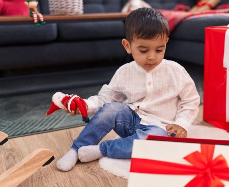 Foto de Adorable niño hispano desempacando regalo de Navidad sentado en el suelo en casa - Imagen libre de derechos
