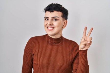 Téléchargez les photos : Non binary person wearing make up standing over isolated background smiling with happy face winking at the camera doing victory sign. number two. - en image libre de droit