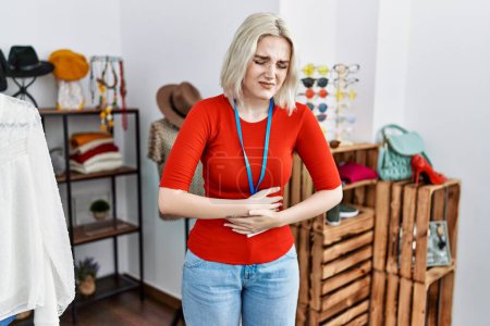 Foto de Young caucasian woman working as manager at retail boutique with hand on stomach because nausea, painful disease feeling unwell. ache concept. - Imagen libre de derechos