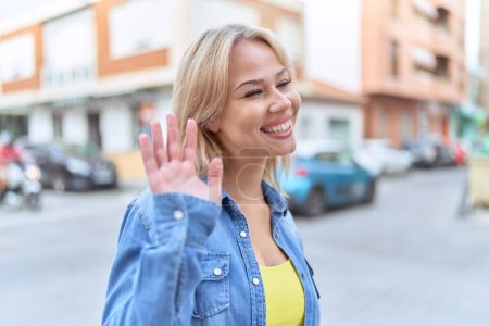 Téléchargez les photos : Jeune femme blonde souriante confiante disant bonjour à la rue - en image libre de droit