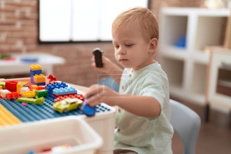 Foto de Adorable niño jugando con bloques de construcción sosteniendo el coche en el jardín de infantes - Imagen libre de derechos