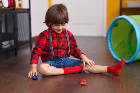 Foto de Adorable niño jugando con coches juguete sentado en el suelo en casa - Imagen libre de derechos