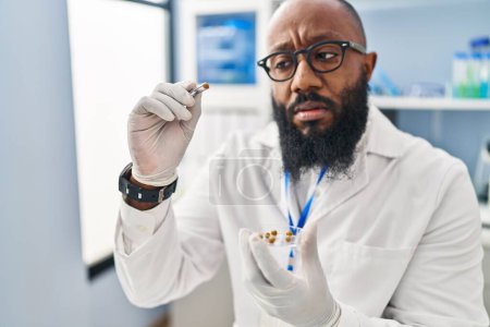 Téléchargez les photos : Jeune homme afro-américain portant un uniforme scientifique à l'aide d'une pince à épiler au laboratoire - en image libre de droit