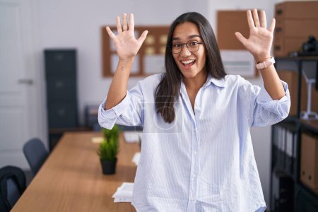Téléchargez les photos : Jeune femme hispanique au bureau montrant et pointant vers le haut avec les doigts numéro dix tout en souriant confiant et heureux. - en image libre de droit