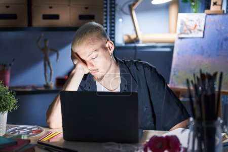 Photo for Young caucasian man using laptop at night at art studio tired rubbing nose and eyes feeling fatigue and headache. stress and frustration concept. - Royalty Free Image