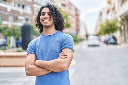 Téléchargez les photos : Jeune homme latino debout les bras croisés dans la rue - en image libre de droit