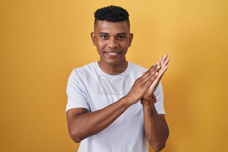 Téléchargez les photos : Jeune homme hispanique debout sur fond jaune applaudissant et applaudissant heureux et joyeux, souriant mains fiers ensemble - en image libre de droit