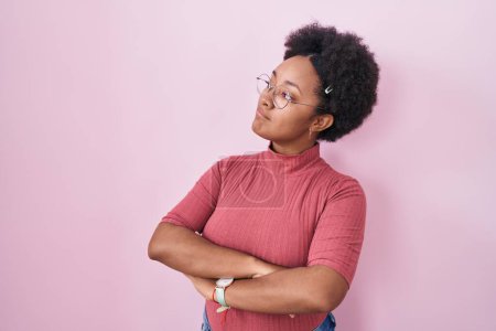 Photo for Beautiful african woman with curly hair standing over pink background looking to the side with arms crossed convinced and confident - Royalty Free Image