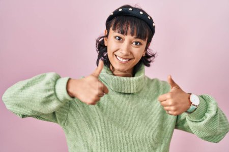 Téléchargez les photos : Young beautiful woman standing over pink background approving doing positive gesture with hand, thumbs up smiling and happy for success. winner gesture. - en image libre de droit