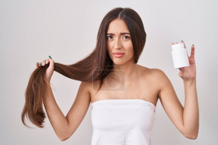 Photo for Young hispanic woman holding hair with hand and pills clueless and confused expression. doubt concept. - Royalty Free Image