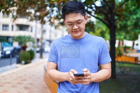 Foto de Young chinese man smiling confident using smartphone at park - Imagen libre de derechos