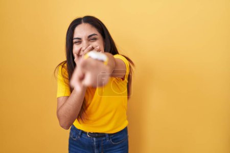 Téléchargez les photos : Jeune femme arabe debout sur fond jaune se moquant de vous, pointant du doigt la caméra avec la main sur la bouche, expression de honte - en image libre de droit