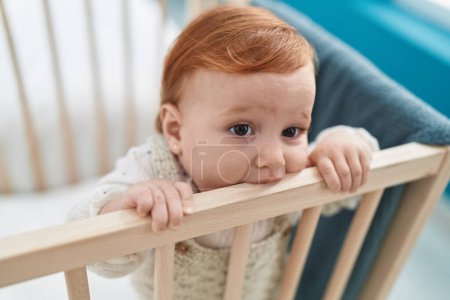 Photo for Adorable redhead toddler bitting cradle standing at bedroom - Royalty Free Image