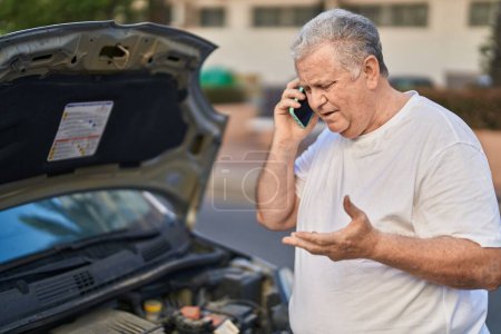 Photo for Middle age grey-haired man talking on smartphone checking car motor at street - Royalty Free Image