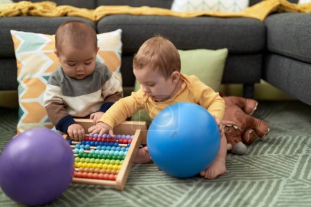 Foto de Dos niños jugando con pelotas y ábaco sentados en el suelo en casa - Imagen libre de derechos