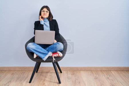 Téléchargez les photos : Jeune femme hispanique assise sur une chaise en utilisant un ordinateur portable touchant la bouche avec la main avec une expression douloureuse à cause de maux de dents ou de maladies dentaires sur les dents. concept de dentiste. - en image libre de droit