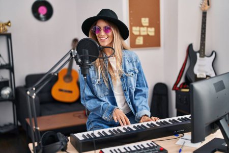 Foto de Young woman musician singing song playing piano keyboard at music studio - Imagen libre de derechos