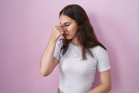 Foto de Young hispanic girl standing over pink background tired rubbing nose and eyes feeling fatigue and headache. stress and frustration concept. - Imagen libre de derechos