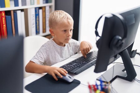 Téléchargez les photos : Adorable élève en bas âge utilisant un ordinateur assis sur la table en classe - en image libre de droit